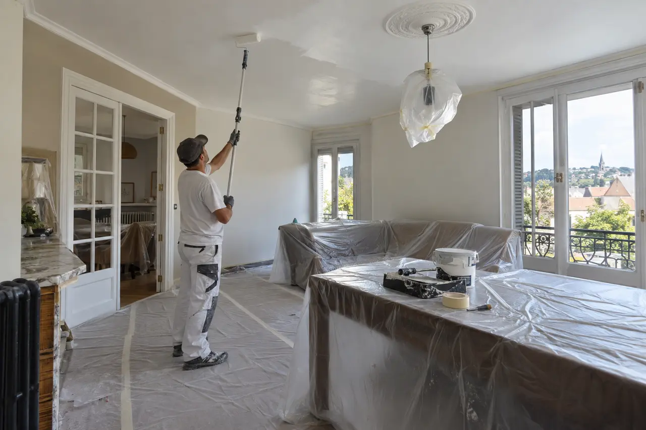 Peintre appliquant une peinture au plafond dans une pièce protégée